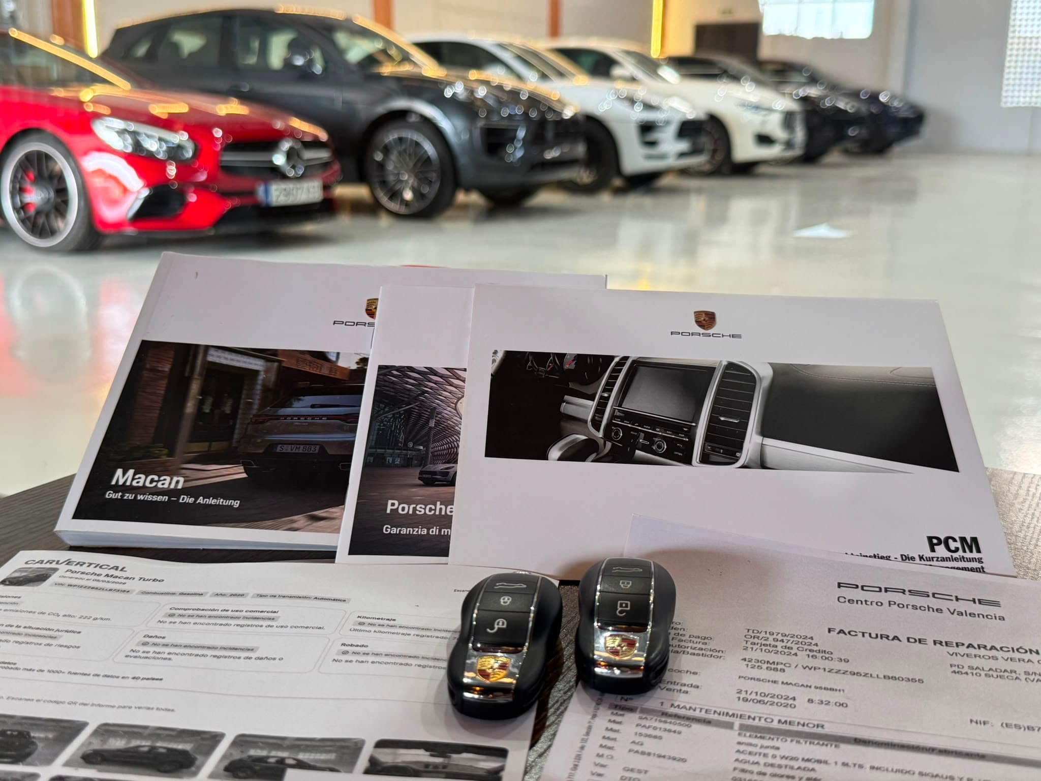 Documentación y llaves de un Porsche con varios vehículos seleccionados al fondo