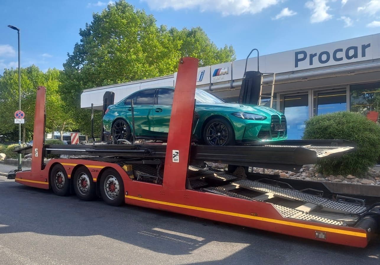 BMW verde cargado en un portacoches frente a las instalaciones de origen