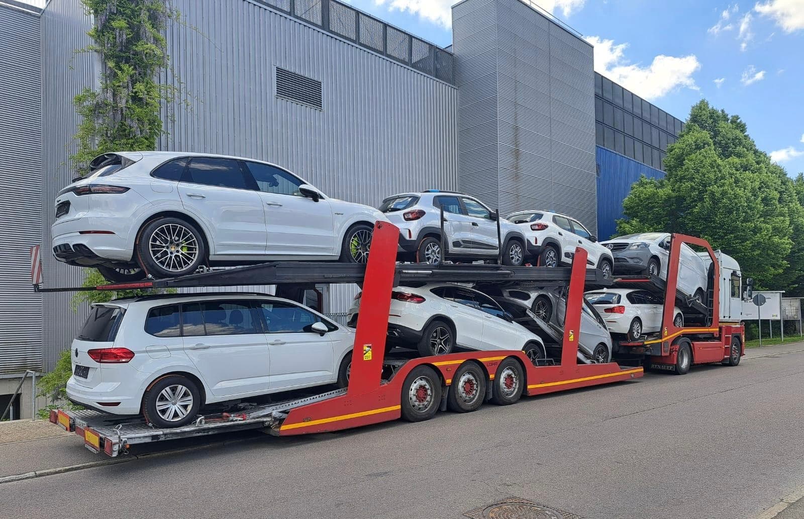 Portacoches cargado con varios vehículos junto a una nave industrial